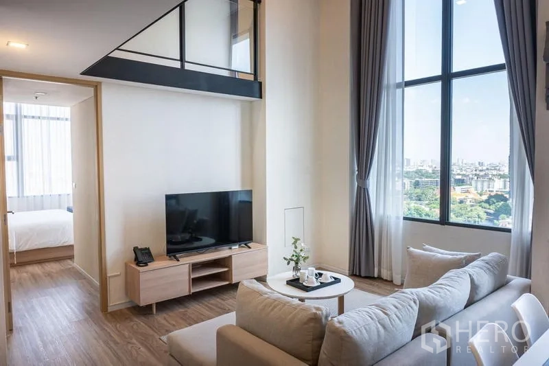 Condominium for rent in Khlong Toei, Bangkok - Living area with panoramic city view through tall windows and a doorway to the bedroom.