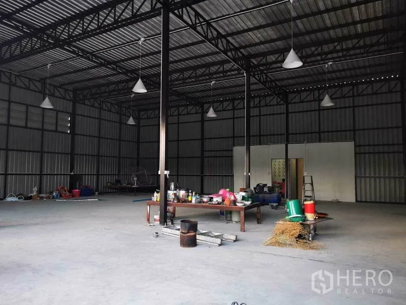 Warehouse for rent - Wide interior shot with multiple hanging lights, a workbench and large open storage area.