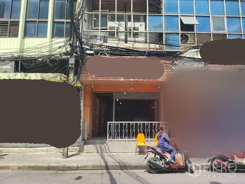 店屋 出租在Khlong Toei, Bangkok - 临街商铺外立面，卷帘门与小前廊，门前停有摩托车。