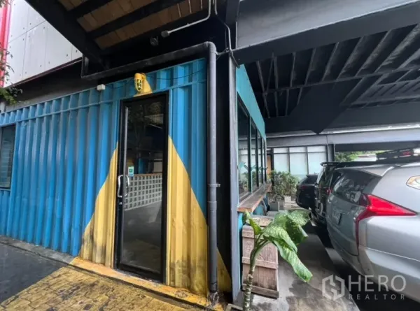 Retail Space for rent - Exterior of blue container retail unit with glass door beside covered parking bays in Ekkamai.