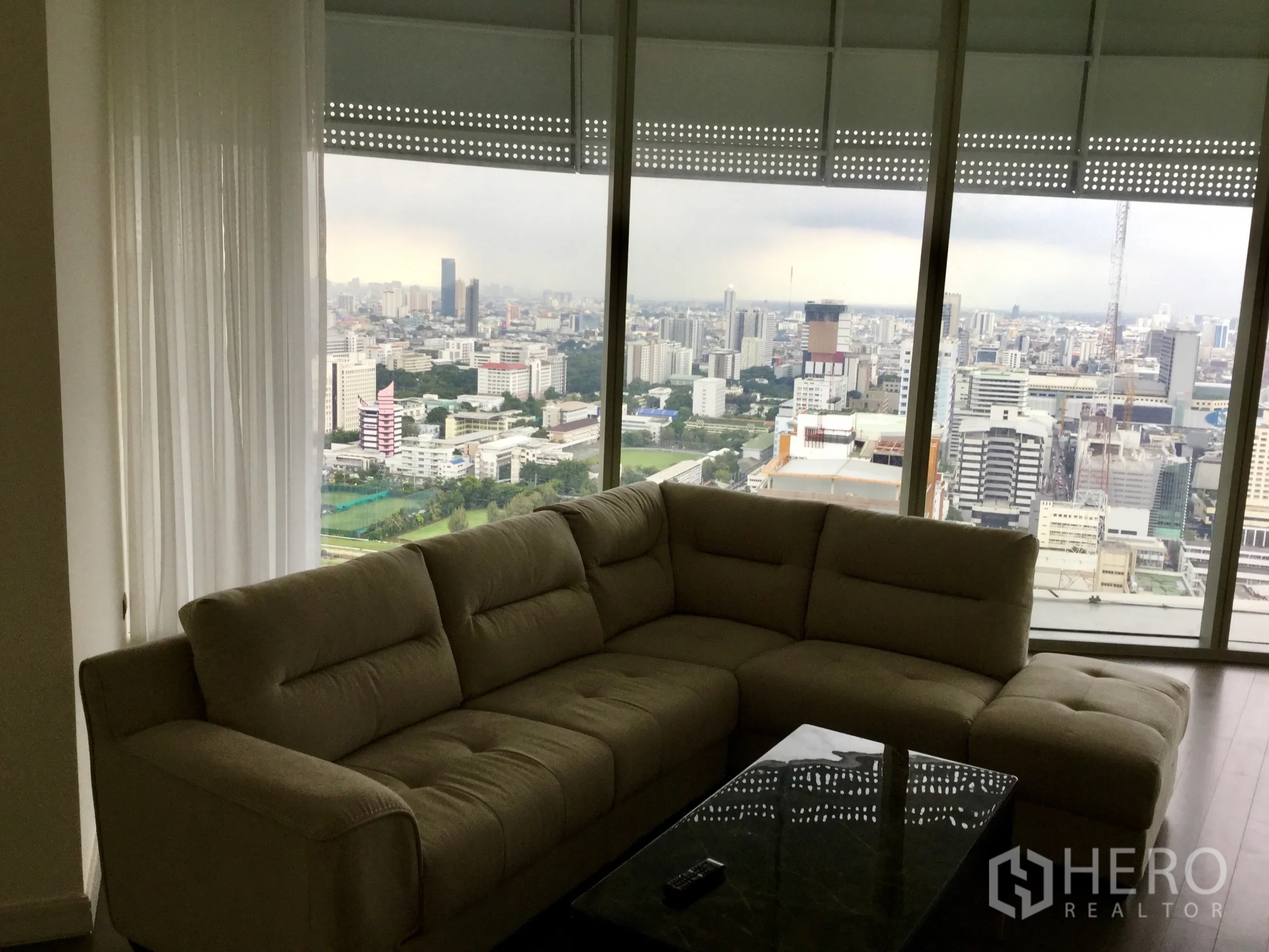 Condominium for rent in Pathum Wan, Bangkok - Bright living room with a large sectional sofa and floor-to-ceiling windows overlooking the Bangkok skyline and golf course.