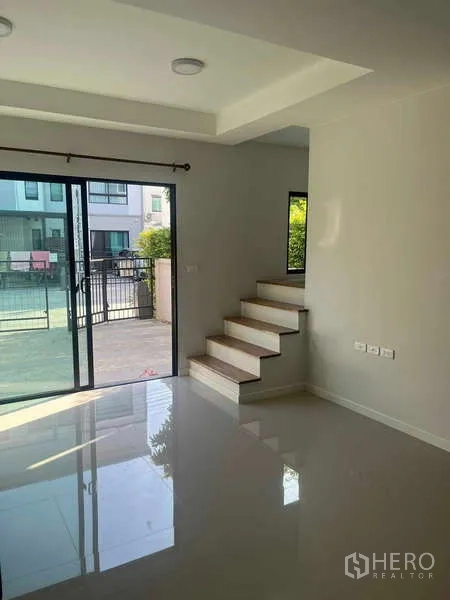 Townhouse for rent in Suan Luang, Bangkok - Living room with staircase, large sliding doors to the front terrace and polished tile flooring.