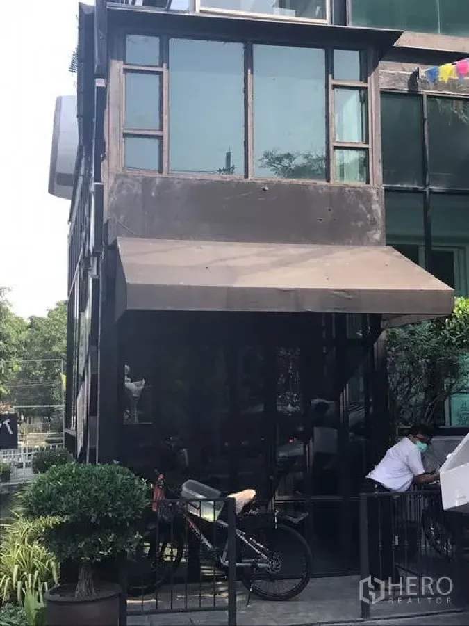 Retail Space for rent in Watthana, Bangkok - Modern glass-fronted retail unit with black metal frame, awning, and greenery in Thonglor, Watthana.