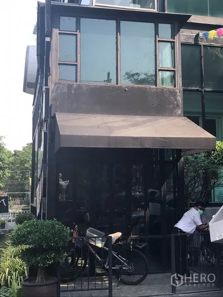 Retail Space for rent in Watthana, Bangkok - Modern glass-fronted retail unit with black metal frame, awning, and greenery in Thonglor, Watthana.