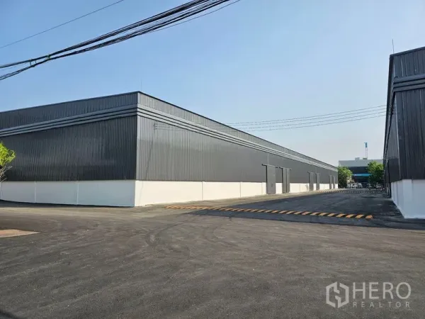 Warehouse for rent in Khlong Toei, Bangkok - Steel-clad warehouse blocks with a wide asphalt driveway and loading zone in an industrial complex.