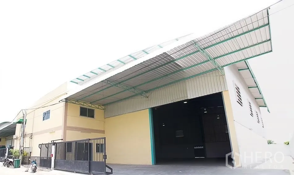Warehouse for rent in Pathum Thani - Warehouse exterior with wide rolling shutter, large covered loading canopy and secure front gate.