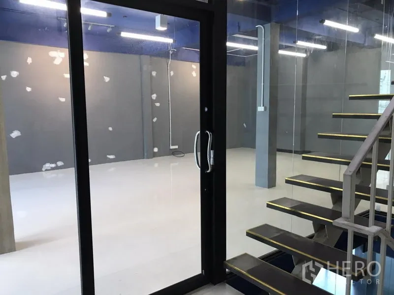 Office Space for rent in Watthana, Bangkok - Glass entry door and floating stairs leading to a bright, grey-walled workspace.