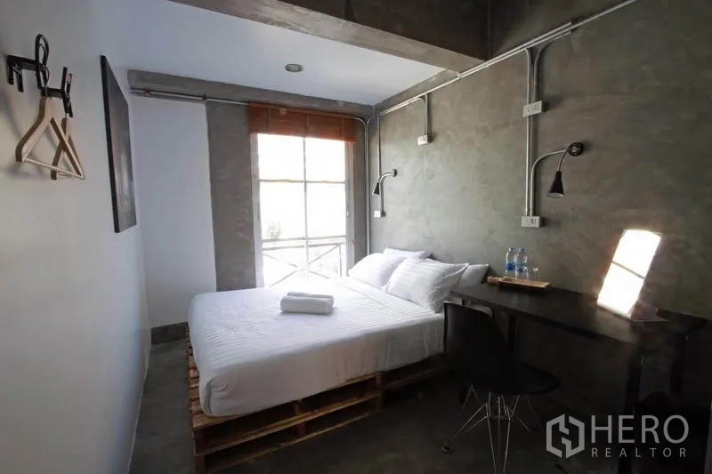 Office Space for rent or sale in Bang Rak, Bangkok - Minimal double bedroom with desk, wall lamps, and a hanging rail.