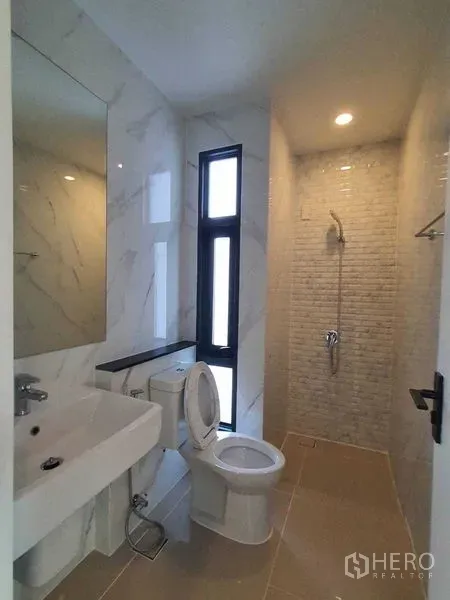 Detached House for sale in Prawet, Bangkok - Compact bathroom with window, sink, toilet, and tiled shower alcove.