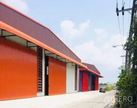 Warehouse for rent in Bueng Kum, Bangkok - Row of modern metal-clad warehouse units with bold orange façades and a wide driveway for truck access.