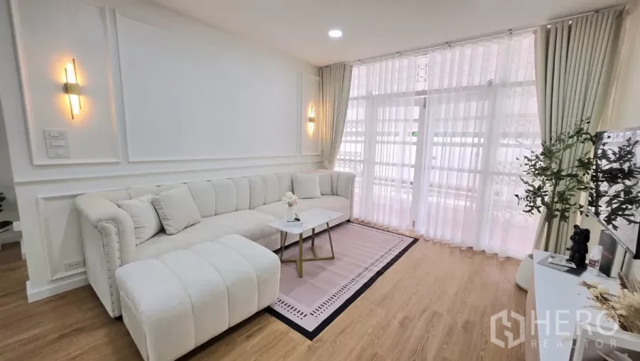 Detached House for rent in Huai Khwang, Bangkok - Bright living room with white L-shaped sofa, wood flooring and sheer curtains in a Huai Khwang, Bangkok detached house.
