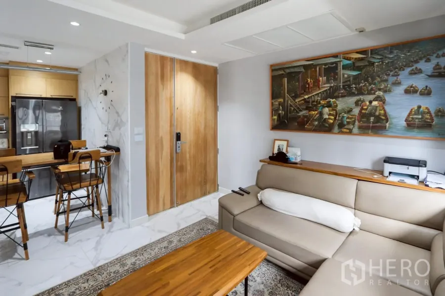 Condominium for rent in Pathum Wan, Bangkok - Bright living room with beige L-shaped sofa, wood coffee table, entry door, dining counter and marble flooring.