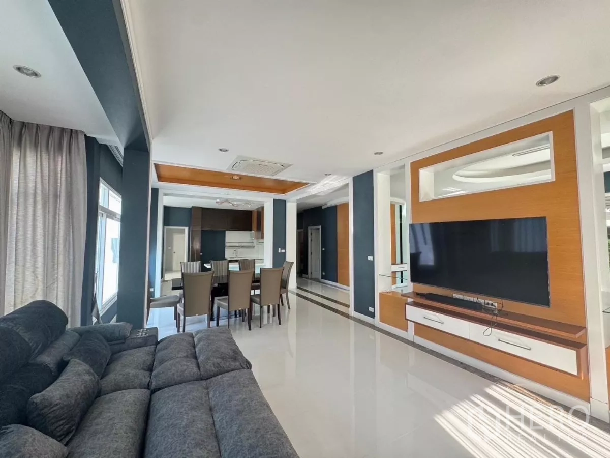 Detached House for rent or sale in Prawet, Bangkok - Open-plan living and dining area with a large sectional sofa and built-in TV wall.