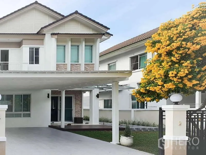 Detached House for rent in Sathon, Bangkok - Two-storey white detached house in Sathon with a covered carport and a blooming yellow tree at the gate.