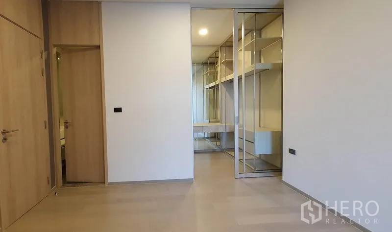 Condominium for sale in Khlong Toei, Bangkok - Master bedroom leading to a mirrored walk-in closet with glass sliding doors.