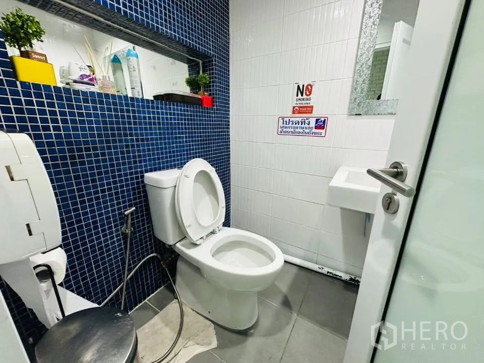 Shophouse for sale in Watthana, Bangkok - Clean restroom with blue mosaic wall tiles, white toilet, and small basin.
