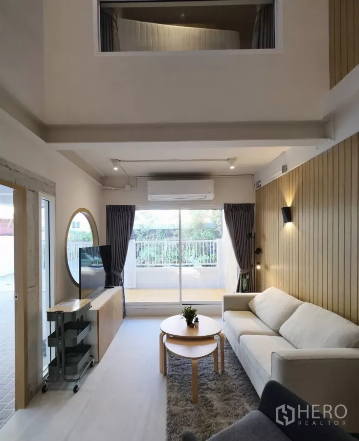 Townhouse for rent or sale in Watthana, Bangkok - Double-height living room with sofa, TV console and sliding doors to terrace.