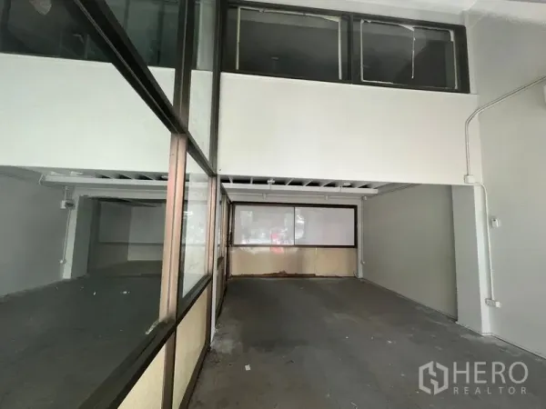 Shophouse for rent in Khlong Toei, Bangkok - Wide ground-floor retail bay with mezzanine windows and a glass-partitioned room at the rear.