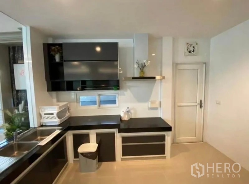 Detached House for rent or sale in Bang Phli, Samut Prakan - Fitted closed kitchen with black countertops, upper cabinets, stainless sink and side door.