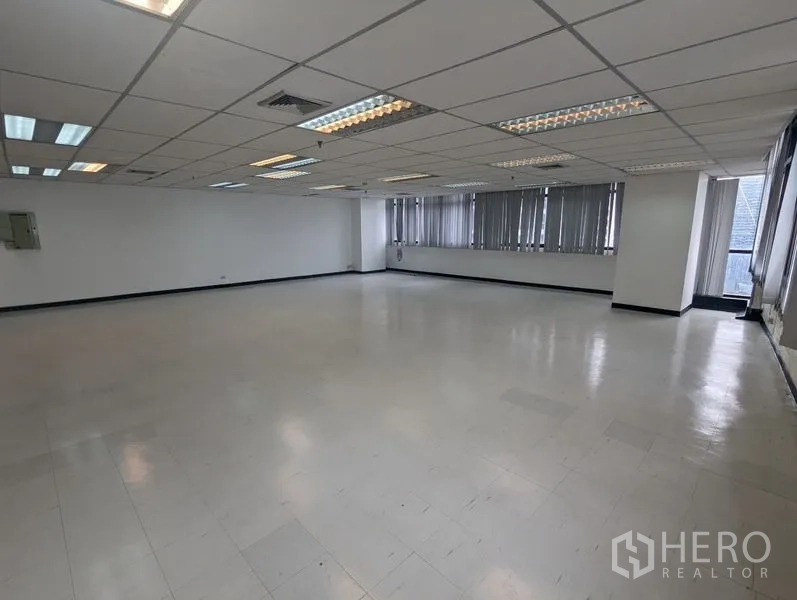 Office Space for rent or sale - Large empty office area with multiple ceiling light panels, AC vents, and wraparound windows providing natural light.