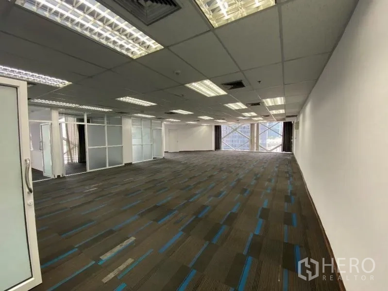 Office Space for rent in Khlong Toei, Bangkok - Long office floor with grid ceiling, AC vents and large cross-braced windows beside frosted glass partitions with city outlook.
