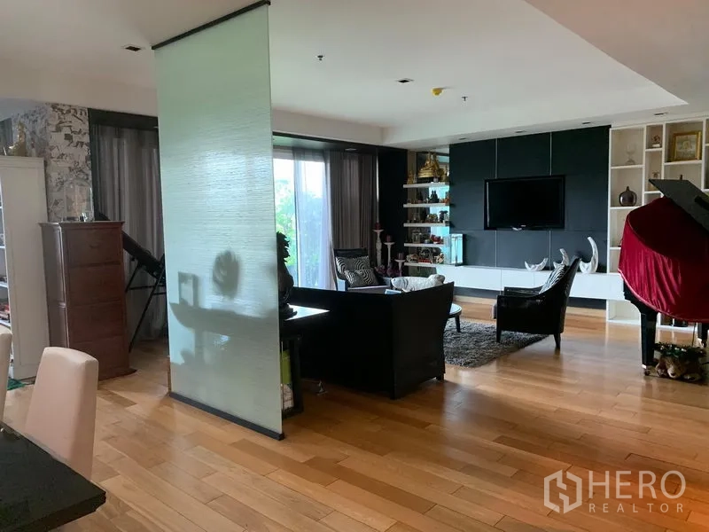 Condominium for sale in Khlong Toei, Bangkok - Open-plan living area with wood floors, TV wall, shelving and sliding glass to the balcony.