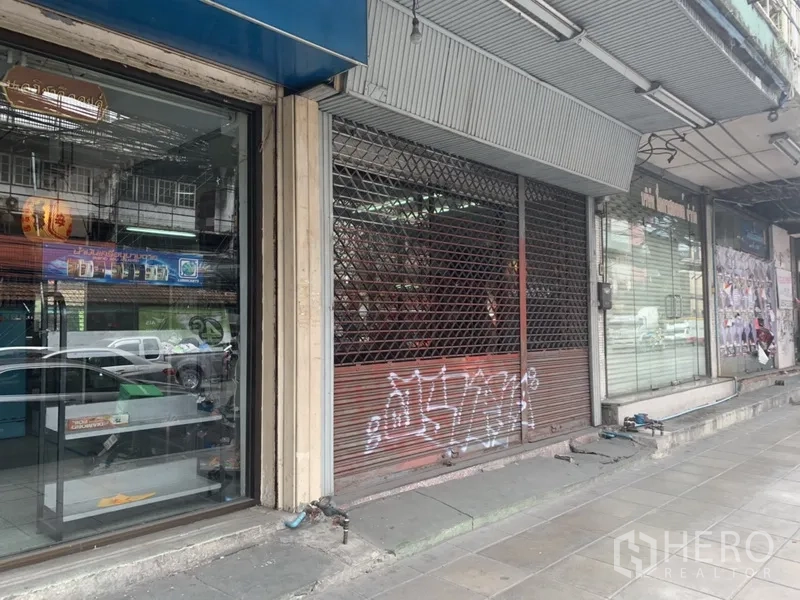 Shophouse for rent in Khlong Toei, Bangkok - Street-level shopfront with metal roller grille and glass panels beneath an awning along the sidewalk.