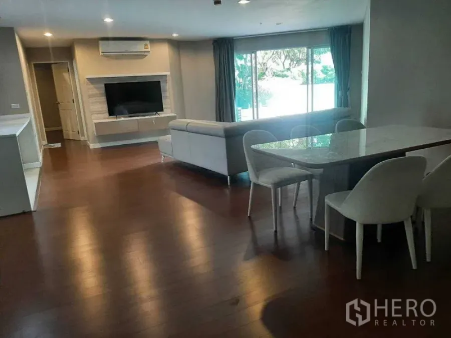 Condominium for rent or sale in Huai Khwang, Bangkok - Open-plan living and dining room with sofa, wall-mounted TV and large window.