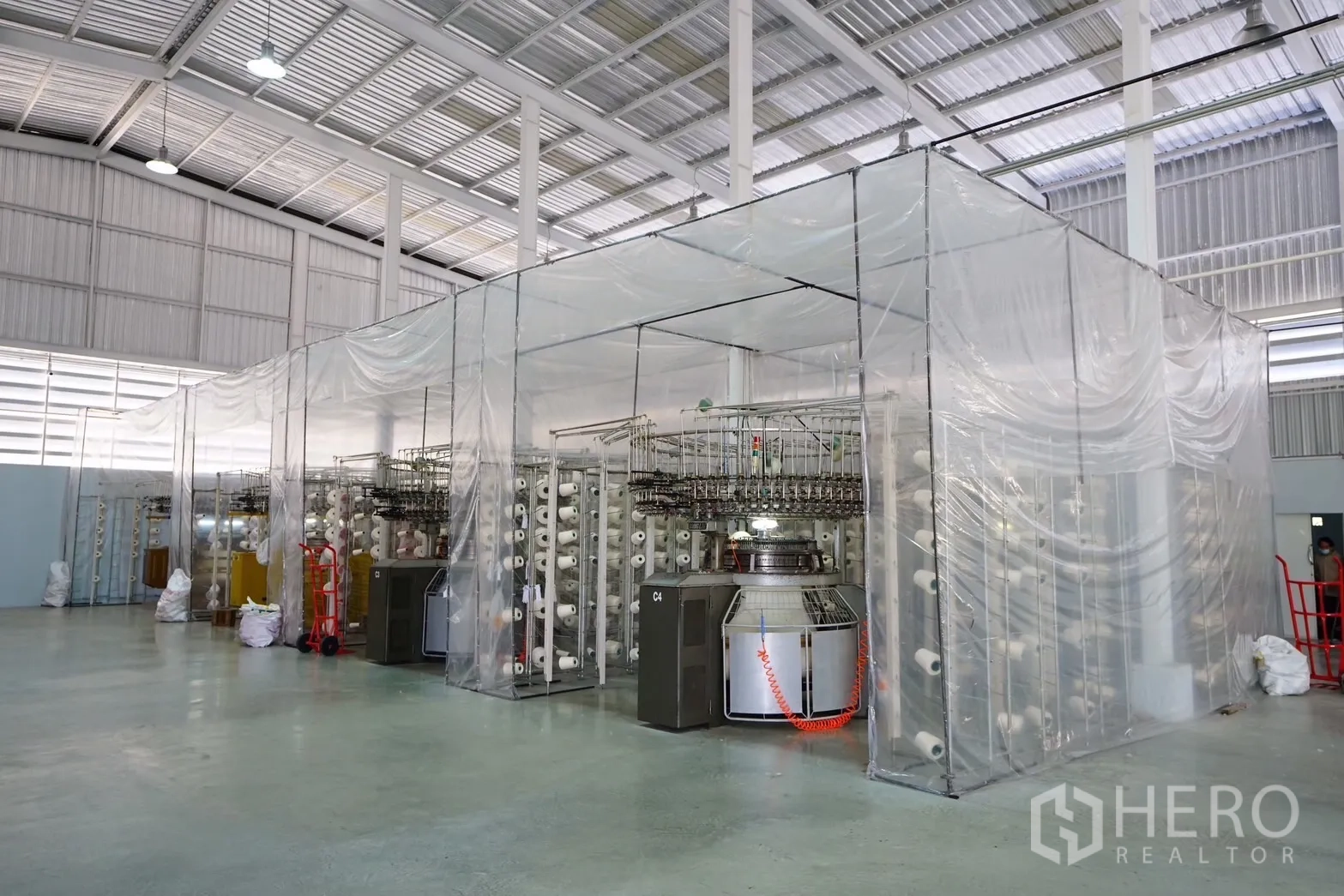 Factory for sale in Krathum Baen, Samut Sakhon - Row of textile machines enclosed by clear plastic curtains in a clean workshop.