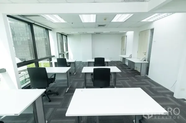 Office Space for rent - Open office area with arranged desks and chairs beside full-height windows and clean white walls.