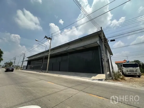 Warehouse for rent in Lam Luk Ka, Pathum Thani - Street-facing metal warehouse exterior with wide sliding doors and loading apron in Lam Luk Ka.