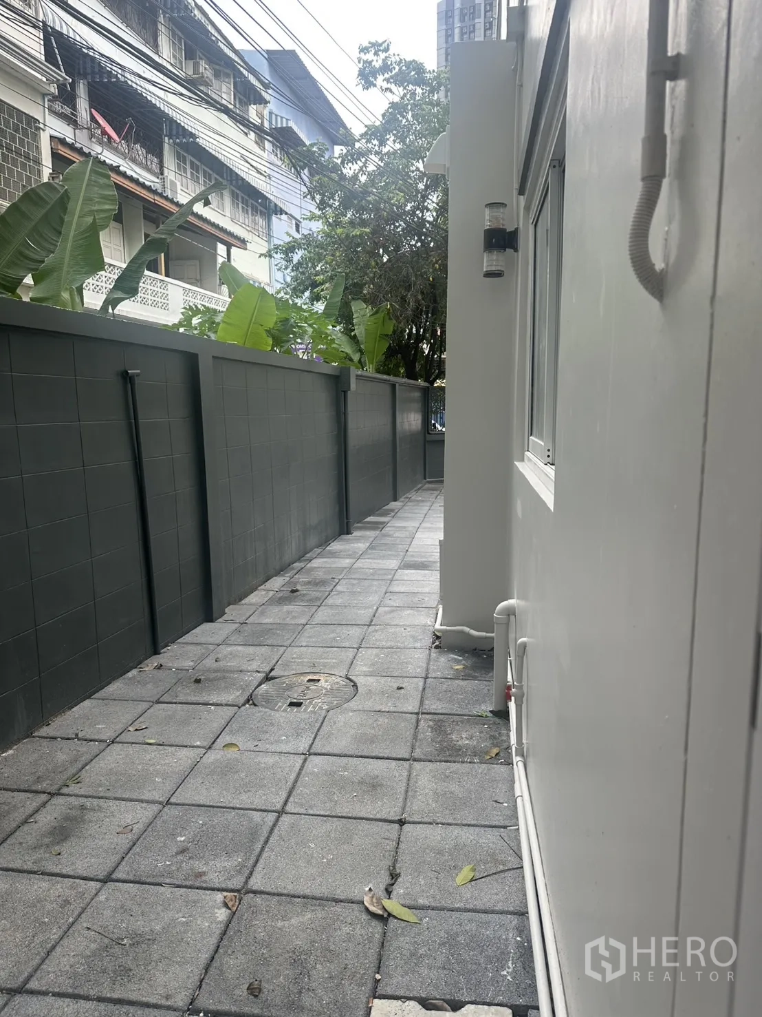 Home Office for rent in Khlong Toei, Bangkok - Side pathway along privacy wall with city wires above.