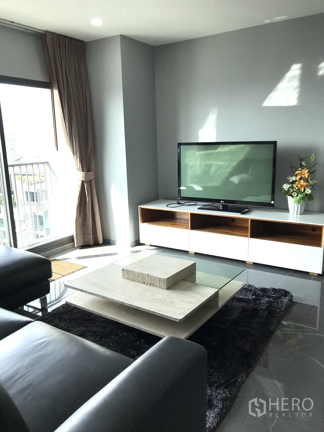 Condominium for rent in Khlong Toei, Bangkok - Living room with TV console and modern glass coffee table on a dark rug.