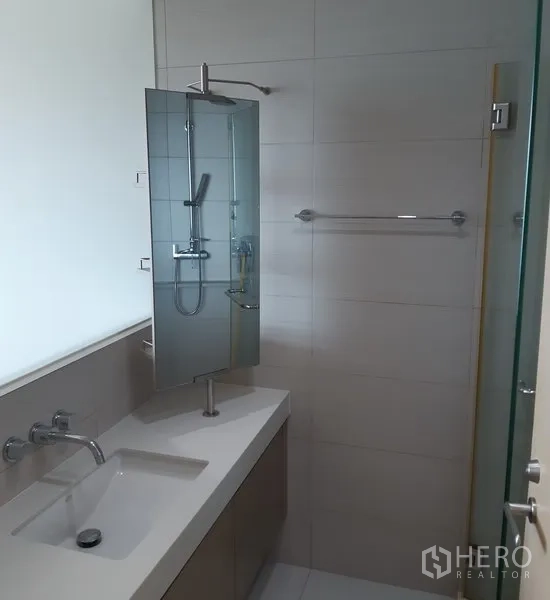 Condominium for sale in Khlong Toei, Bangkok - Contemporary bathroom with long vanity, mirror and glass-enclosed shower.