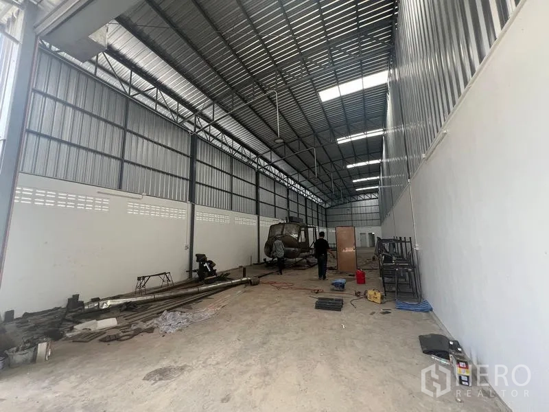 Warehouse for rent in Khlong Sam Wa, Bangkok - Deep storage bay inside the warehouse featuring a high ceiling, skylights and durable concrete flooring with equipment stacked along the sides.