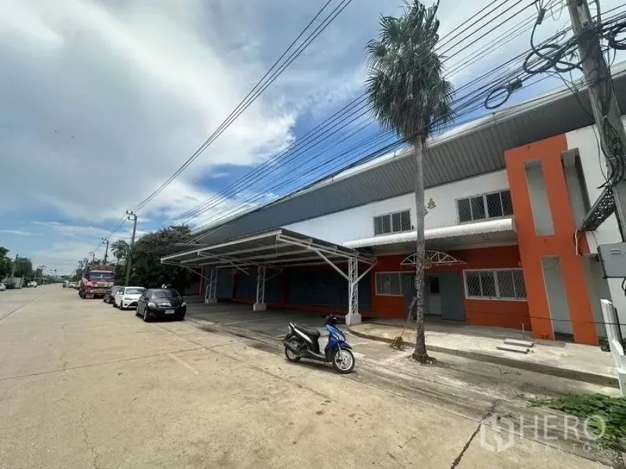 Factory for rent in Nonthaburi - Side frontage of the factory with covered bay, palm tree and easy truck access along the road.