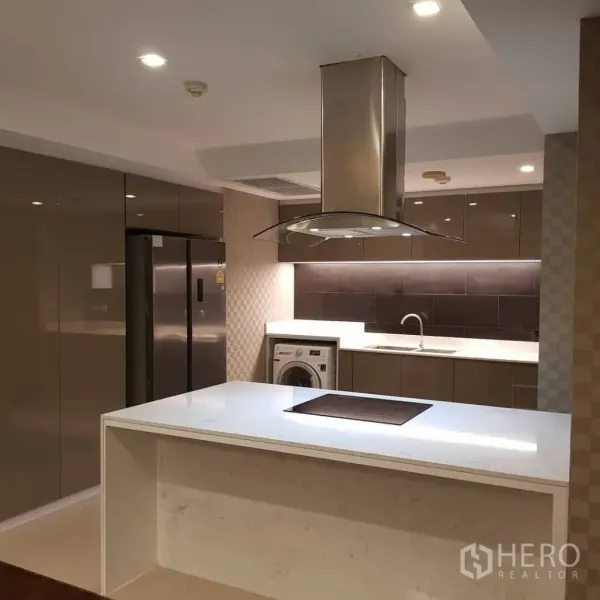 Condominium for rent or sale in Pathum Wan, Bangkok - Contemporary kitchen featuring a white island with cooktop, stainless range hood, fridge, and built-in washer.