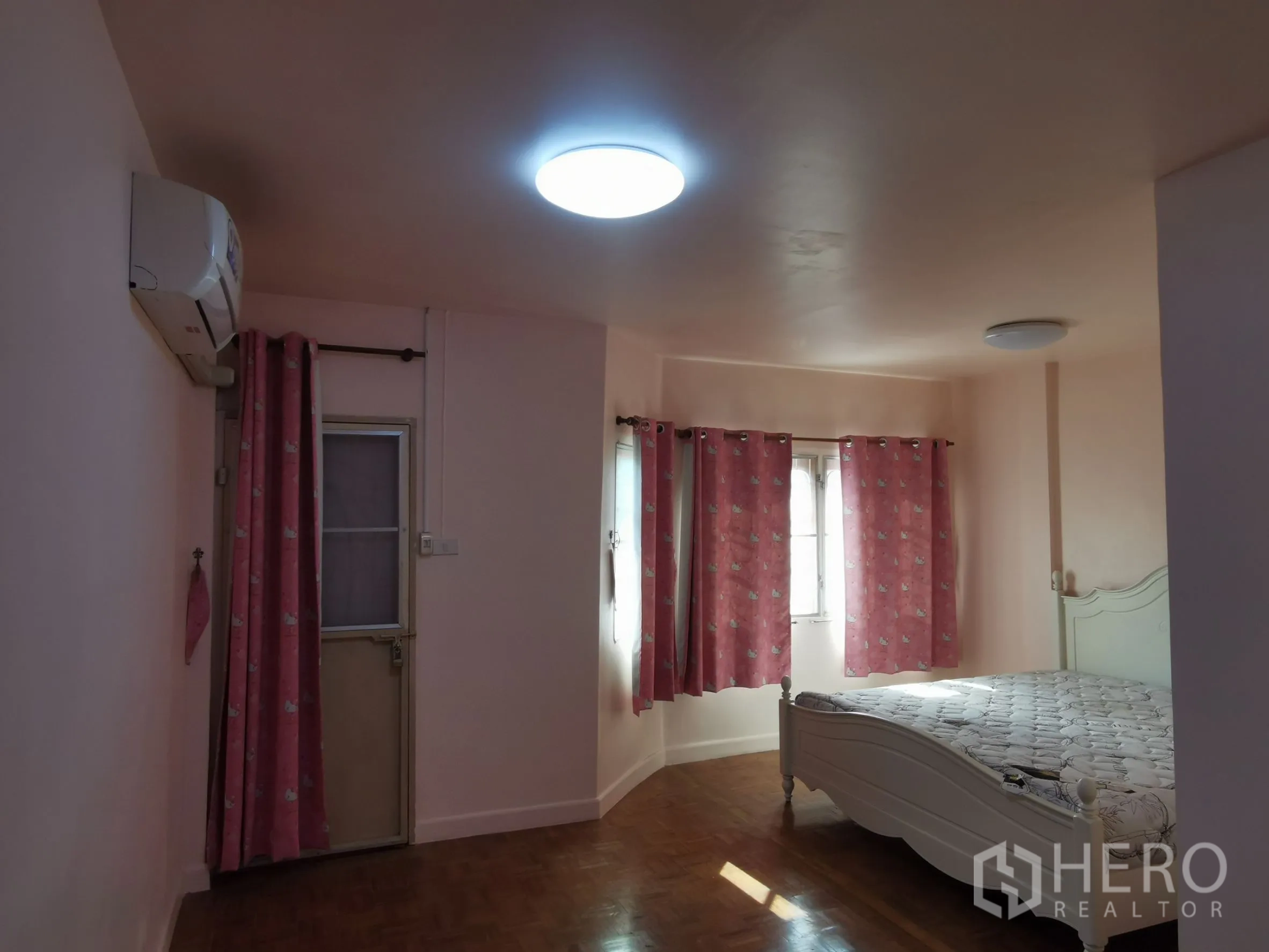 Townhouse for rent in Khlong Toei, Bangkok - Master bedroom with AC, multiple windows, and a white bed frame with pink curtains.