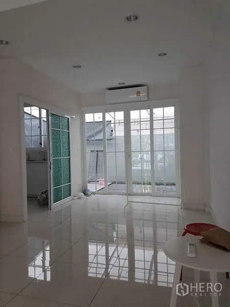 Townhouse for rent in Bang Na, Bangkok - Bright ground-floor room with white tile floors, sliding glass doors and air conditioning opening to the patio.