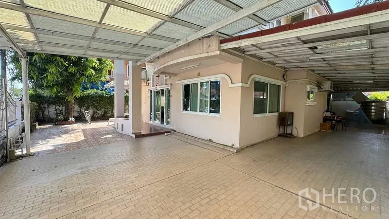 Detached House for sale in Mueang Pathum Thani, Pathum Thani - Covered carport and front patio of a two-storey detached house with paved driveway and garden greenery.