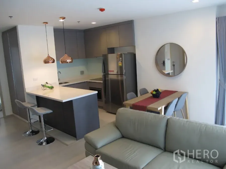 Condominium for rent or sale in Khlong Toei, Bangkok - Open-plan condo kitchen with island, copper pendant lights, dining nook and sofa.