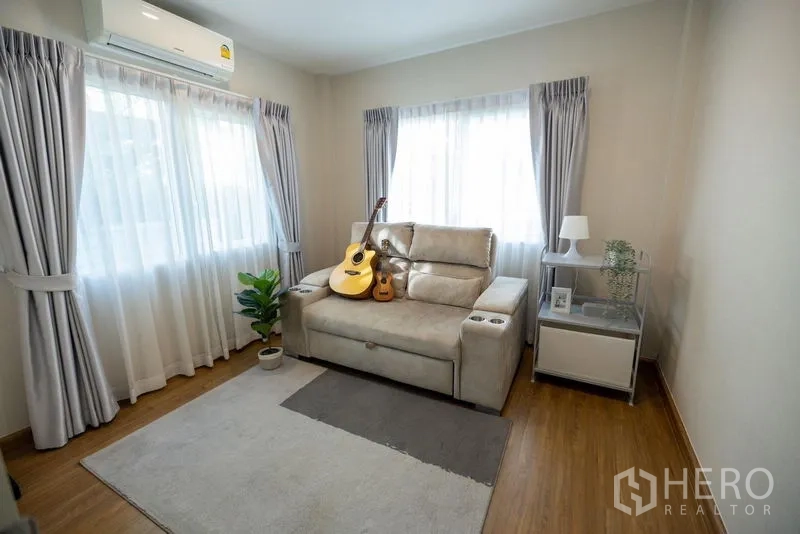 Detached House for sale in Prawet, Bangkok - Cozy living room with sofa, rug and large windows, decorated with guitars.
