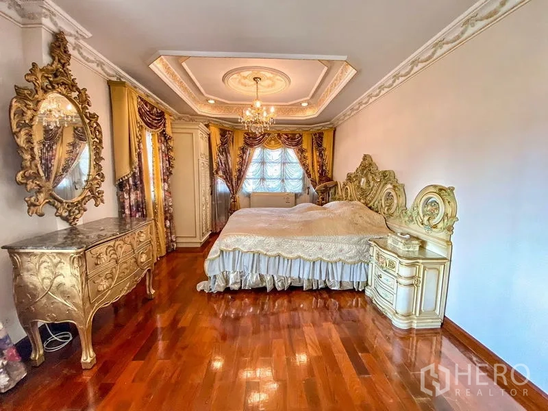 Detached House for rent or sale in Bang Khen, Bangkok - Master bedroom with carved headboard, chandeliers, and polished wood flooring.