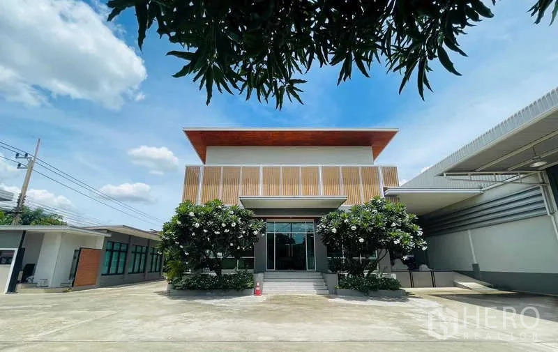 Factory for sale in Krathum Baen, Samut Sakhon - Front facade of the office building with glass entrance, steps, and frangipani landscaping.