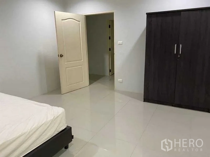 Home Office for rent in Khlong Toei, Bangkok - Large bedroom with bed, wardrobe and white door on polished tile flooring.