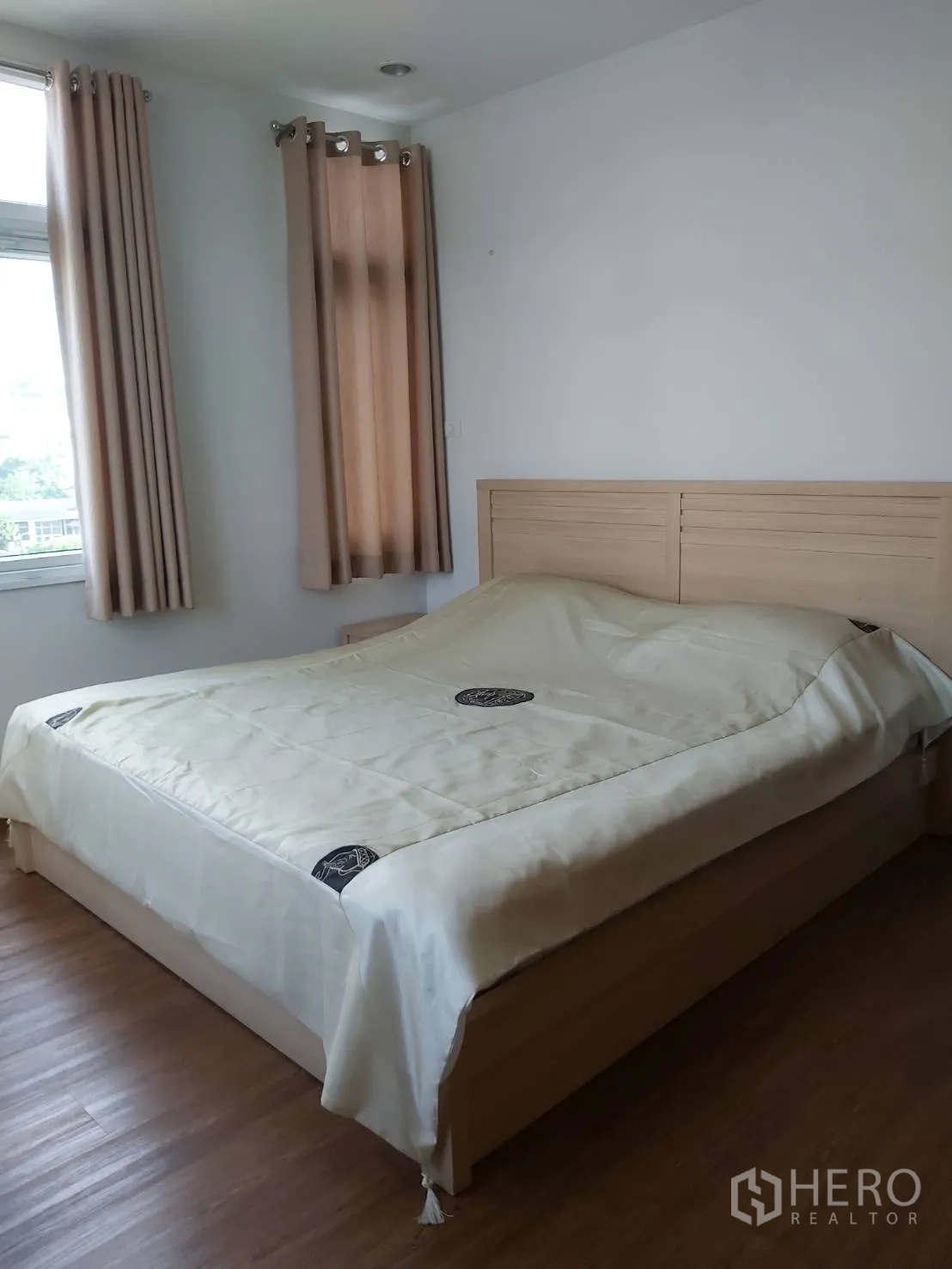Apartment for rent in Khlong Toei, Bangkok - Primary bedroom with double bed, wood flooring, and two windows with beige curtains.