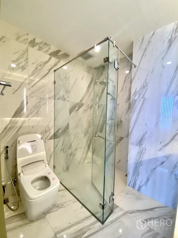 Condominium for sale in Pathum Wan, Bangkok - Bathroom with glass-enclosed rain shower and modern toilet on marble floors and walls.