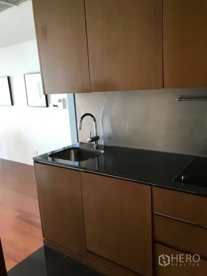 Condominium for rent in Pathum Wan, Bangkok - Compact kitchenette with wood cabinets, black granite countertop and stainless backsplash.