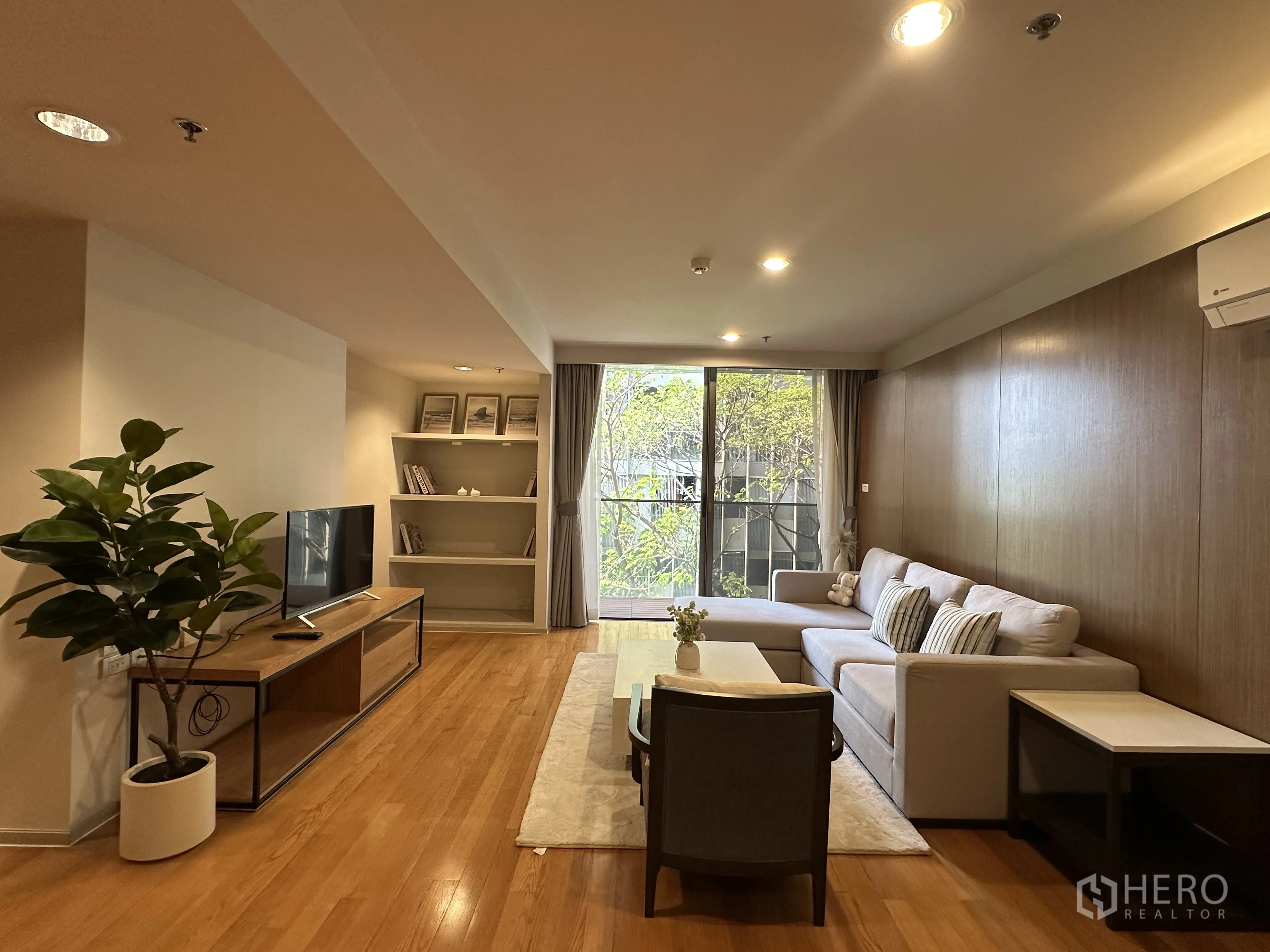 Condominium for rent in Khlong Toei, Bangkok - Spacious living room with L-shaped sofa, TV console, and access to the balcony.