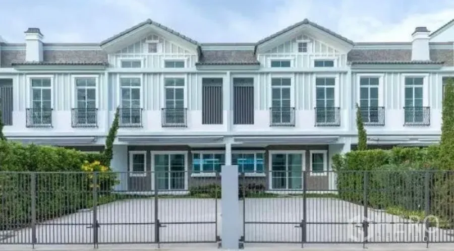 Townhouse for rent in Prawet, Bangkok - Front facade of a modern two-story white townhouse with gated driveway and trimmed hedges.